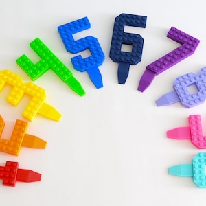 May include: A set of ten colorful plastic number candles, each shaped like a number from one to ten. The candles are arranged in a semi-circle on a white background. The candles are made to look like Lego bricks.