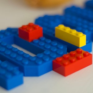 May include: A close-up of blue, yellow, and red Lego blocks. The blocks are arranged in a pattern, with the blue blocks forming a base and the yellow and red blocks stacked on top.