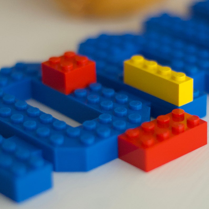 May include: A close-up of blue, yellow, and red Lego blocks. The blocks are arranged in a pattern, with the blue blocks forming a base and the yellow and red blocks stacked on top.