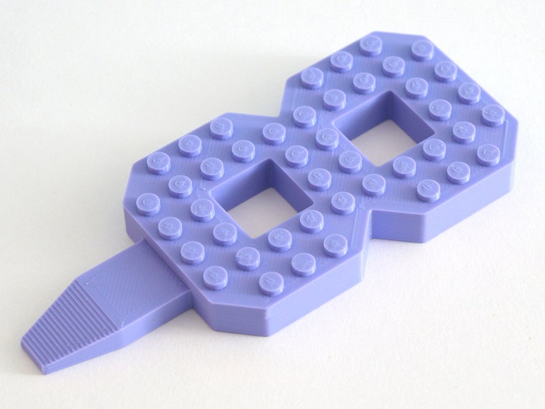 May include: A purple plastic number eight made from Lego bricks. The number eight has a small handle on the bottom.