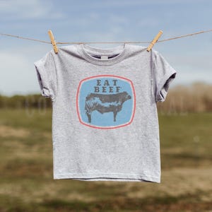 May include: A gray t-shirt with a blue and red graphic of a cow and the text "EAT BEEF".