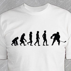 May include: White t-shirt with a black silhouette of the evolution of man, ending with a hockey player.