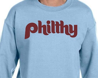 May include: A light blue sweatshirt with a maroon "philthy" graphic printed on the front.
