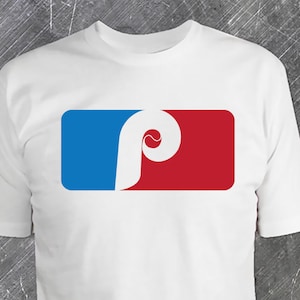 May include: White t-shirt with a red, white, and blue baseball logo. The logo features a white letter "P" with a baseball inside the letter.