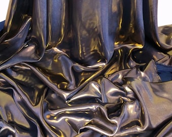 May include: A close-up of a metallic gold fabric with a subtle shimmer. The fabric is draped and folded, creating soft, flowing lines.