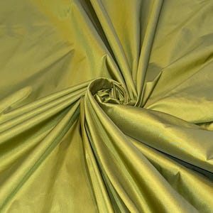 Puede incluir: Primer plano de una tela suave y sedosa de color verde apagado. La tela está drapeada y doblada, creando líneas suaves y fluidas.