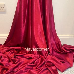 Puede incluir: Una tela de satén rojo oscuro con una textura suave y sedosa. La tela está drapeada y doblada, mostrando su tacto lujoso.