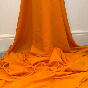 May include: A bright orange fabric backdrop, ideal for photography or crafting projects. The fabric is smooth and wrinkle-free, providing a clean and professional look.
