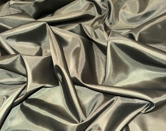 Può includere: Primo piano di un tessuto dall'aspetto lucido e brillante. Il tessuto è di un verde oliva tenue, con pieghe e piegature che creano luci e ombre. Il materiale appare liscio e fluido, suggerendo un tessuto lussuoso.