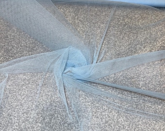 May include: Light blue tulle fabric, rolled and spread out. The fine mesh material is semi-transparent, with a soft, airy appearance. The fabric is a solid, pale blue color, suitable for various craft and design projects.