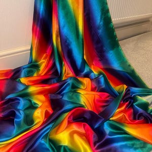 Puede incluir: Tela satinada con los colores del arcoíris. Presenta un degradado de colores que va del rojo al violeta, con reflejos brillantes. La tela está drapeada, creando pliegues suaves y un efecto brillante, ideal para confección.