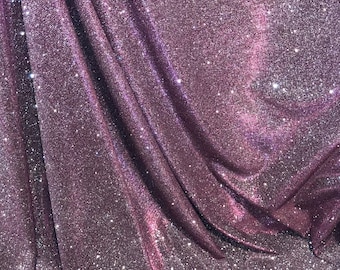 Könnte beinhalten: Eine Nahaufnahme eines glitzernden, schillernden Stoffes mit einem violetten Farbton. Der Stoff hat eine feine, glitzernde Textur und ist in weichen Falten drapiert.