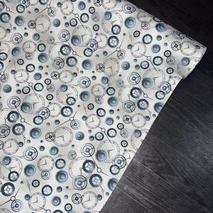 Könnte beinhalten: Eine Stoffrolle mit einem sich wiederholenden Muster aus Uhren und Zahnrädern in Grau- und Blautönen. Das Design umfasst Zifferblätter mit Zeigern sowie verschiedene Zahnradformen, die eine Steampunk- oder industrielle Ästhetik erzeugen.