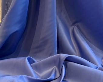 Può includere: Primo piano di un tessuto blu reale drappeggiato e lucido. Il tessuto ha una consistenza liscia con sottili linee verticali e pieghe, che creano ombre e riflessi. Il colore è un blu intenso e saturo.