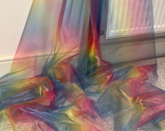 Op de afbeelding: Een doorschijnende stof met een regenboogkleurverloop, van rood tot violet. De stof is gedrapeerd en geplooid, waardoor plooien en schaduwen ontstaan. Het materiaal lijkt licht en kan gebruikt worden voor decoratieve doeleinden of kleding.