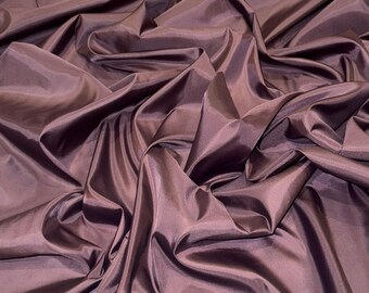 Può includere: Primo piano di un tessuto lussuoso e drappeggiato in un profondo colore prugna. Il materiale ha una consistenza liscia e lucida, con pieghe e ombre che creano profondità. Il tessuto sembra essere un tessuto di alta qualità, adatto all'abbigliamento o all'arredamento.
