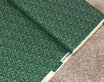 Pode incluir: Tecido verde com um padrão de videira floral branca. O tecido é etiquetado como "Floral Vine International"