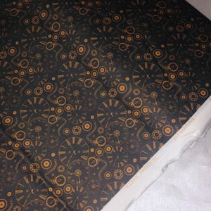 Könnte beinhalten: Schwarzer Stoff mit einem sich wiederholenden Muster aus goldenen Zifferblättern und Zahnrädern. Der Stoff trägt den Text "FABRIC FREEDOM" und "STEAMPUNK".