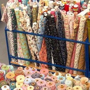 May include: A large collection of fabric rolls in various colors and patterns, including polka dots, stripes, and floral prints. The rolls are stacked on shelves and organized by color.