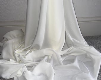 Può includere: Tessuto bianco drappeggiato su un tappeto grigio. Il tessuto è morbido e fluido, con una texture liscia.