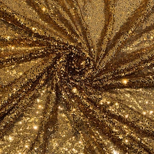 Könnte beinhalten: Ein Stoffmaterial, das mit kleinen, reflektierenden goldenen Pailletten in einem dichten, wirbelnden Muster bedeckt ist. Die Oberfläche weist einen metallischen Glanz auf, wobei das Licht von den einzelnen runden Scheiben reflektiert wird.