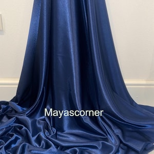 Puede incluir: Un primer plano de una tela de satén azul oscuro. La tela es lisa y brillante, con un ligero brillo. La tela está doblada de una manera que muestra su textura. El texto "Mayascorner" es visible en el centro inferior de la imagen.