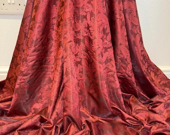 May include: Red paisley patterned fabric with a satin sheen. The fabric is folded and draped on a surface.