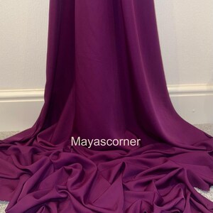 Könnte beinhalten: Ein tiefes lilafarbenes Stoff mit glatter Textur. Der Stoff ist drapiert und gefaltet, was seine fließende Natur zeigt. Der Text "Mayascorner" ist in der Mitte des Bildes sichtbar.