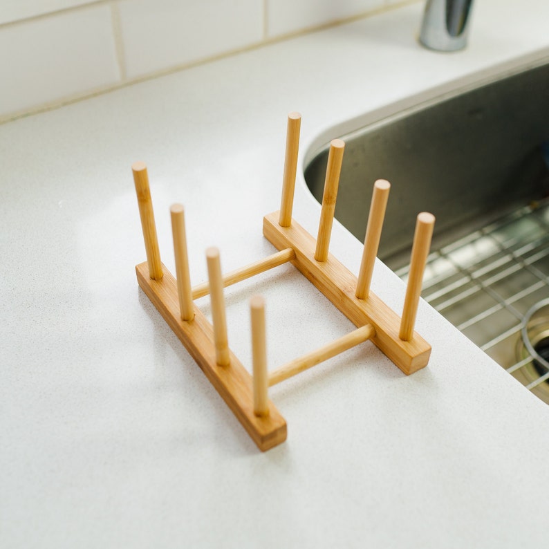 May include: A wooden dish drying rack with six vertical slots for holding plates and bowls. The rack is made of natural bamboo and has a light brown color.