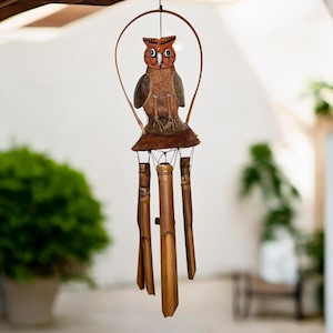 May include: A wooden owl wind chime with brown and orange painted details. The owl is perched on a coconut shell base and hangs from a metal ring. The chime features five bamboo tubes of varying lengths.