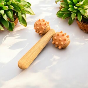 May include: A wooden face roller with two peach-coloured spiked ends. The roller is made of natural bamboo and has a smooth, polished finish.