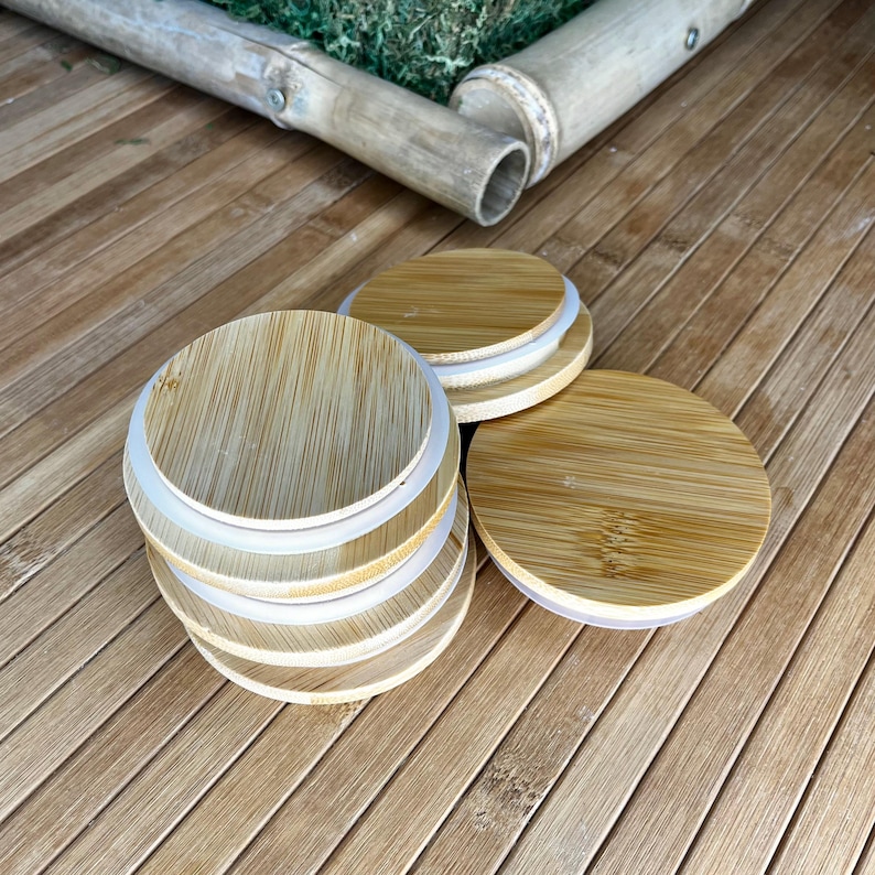 Puede incluir: Una pila de tapas circulares de bamb&uacute; con patrones de vetas de madera de color tostado claro y sellos de silicona blanca en los bordes. Las tapas son planas y redondas, dise&ntilde;adas para recipientes, y est&aacute;n dispuestas junto a una tapa separada.