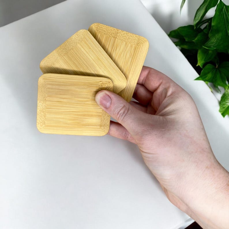 May include: Three rectangular bamboo coasters with rounded corners and a natural light wood grain finish. The coasters are stacked in a staggered arrangement, showcasing the smooth texture and horizontal grain pattern of the bamboo material.