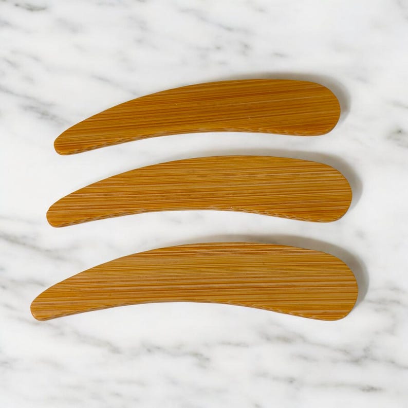 May include: Three curved, elongated wooden tools with a smooth, light brown finish and visible horizontal grain patterns. Each tool features a tapered, rounded end and a wider, slightly curved body, showcasing a natural wood texture throughout.