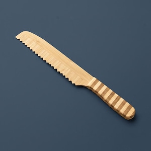 May include: A serrated knife crafted from light-colored bamboo wood. The blade features a sharp, jagged edge for cutting, while the handle displays a distinct pattern of alternating light and dark brown horizontal stripes along its entire length.