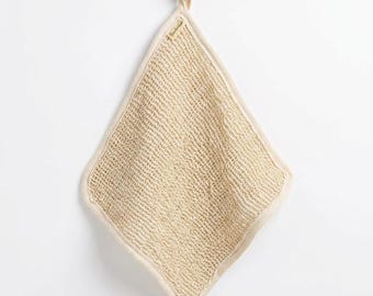 May include: A square-shaped, beige, open-weave textured washcloth with a thick, reinforced border. The cloth features a small, rectangular fabric tag with the text "Bambaw" attached to the top edge, hanging from a small wooden hook.