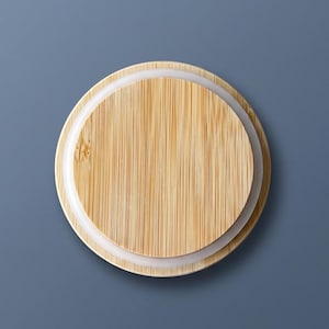 Puede incluir: Una tapa circular de bamb&uacute; con un patr&oacute;n de veta de madera clara natural y l&iacute;neas verticales. La tapa incluye un anillo de sellado de silicona blanca en el borde exterior, dise&ntilde;ado para cerrar herm&eacute;ticamente un recipiente o frasco.