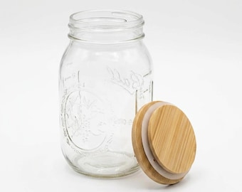 May include: A clear glass mason jar with embossed fruit detailing and the word Ball on the front. The jar features a wide mouth opening and is accompanied by a separate round bamboo lid with a white silicone seal ring for a secure closure.
