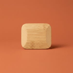 May include: A rectangular bamboo block with rounded corners and a beveled edge. The light tan wood features a visible natural grain pattern running horizontally across the surface, showcasing the organic texture and light brown color of the material.