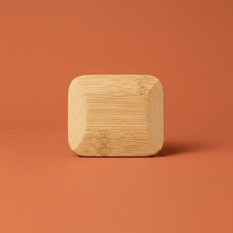 May include: A rectangular bamboo block with rounded corners and a beveled edge. The light tan wood features a visible natural grain pattern running horizontally across the surface, showcasing the organic texture and light brown color of the material.