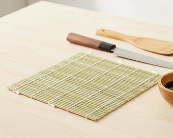 May include: A rectangular bamboo sushi rolling mat made of thin, light green slats held together by white cotton string. Beside the mat lies a stainless steel kitchen knife with a dark brown wooden handle and a light brown wooden spatula.
