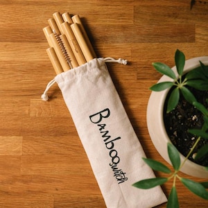 K&ouml;nnte beinhalten: Ein Satz wiederverwendbarer Bambusstrohhalme in einer wei&szlig;en Stofftasche mit dem aufgedruckten Text "Bambooswitch". Die Strohhalme sind geb&uuml;ndelt und beinhalten eine Reinigungsb&uuml;rste.