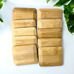 May include: A set of ten rectangular bamboo coasters arranged in two vertical columns of five. Each coaster features a natural light brown wood grain pattern with beveled edges and a smooth, flat surface, showcasing the organic texture of bamboo.