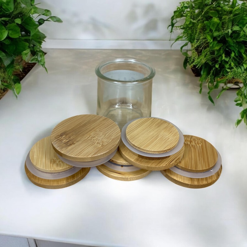 May include: A clear glass jar with a wide opening, accompanied by five circular bamboo lids. Each lid features a natural wood grain pattern and a silicone seal ring around the edge, designed to fit securely onto the top of the glass container.