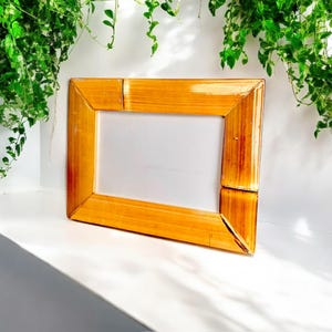 May include: A natural wood picture frame with a light brown finish. The frame is made of bamboo and has a simple, rectangular design.