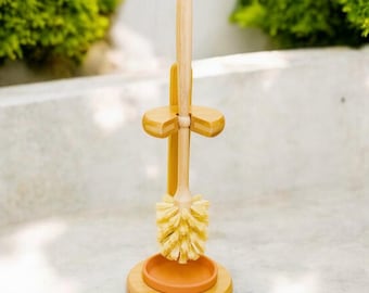 May include: A bamboo toilet brush and holder with a terracotta colored base. The brush has natural bristles and a wooden handle.