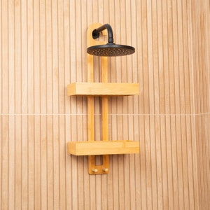 May include: A wooden shower shelf with two tiers and a black shower head. The shelf is mounted on a tiled wall.