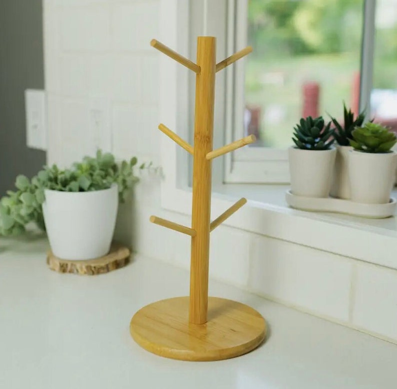 May include: A natural bamboo mug tree stand with six hooks for hanging mugs. The stand has a round base and is made of light brown bamboo.