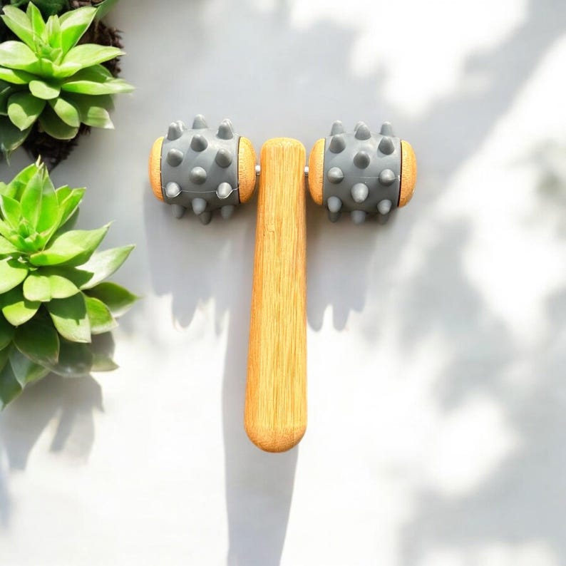 May include: A wooden face roller with two grey spiked rollers. The roller is designed for facial massage.