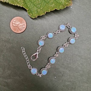 May include: A silver bracelet with a chain link design and round opal stones. The bracelet has a lobster clasp closure.